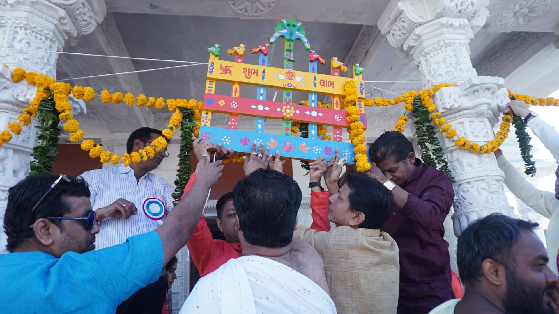Devotees raising the decorated toran at the temple entrance with marigold garlands