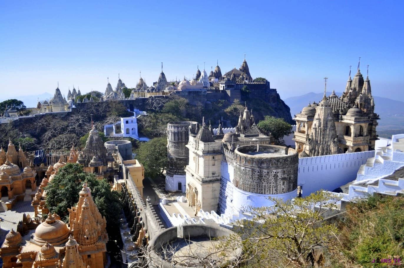 Temple city atop Shatrunjaya hill in Palitana with marble shikhars under a clear blue sky