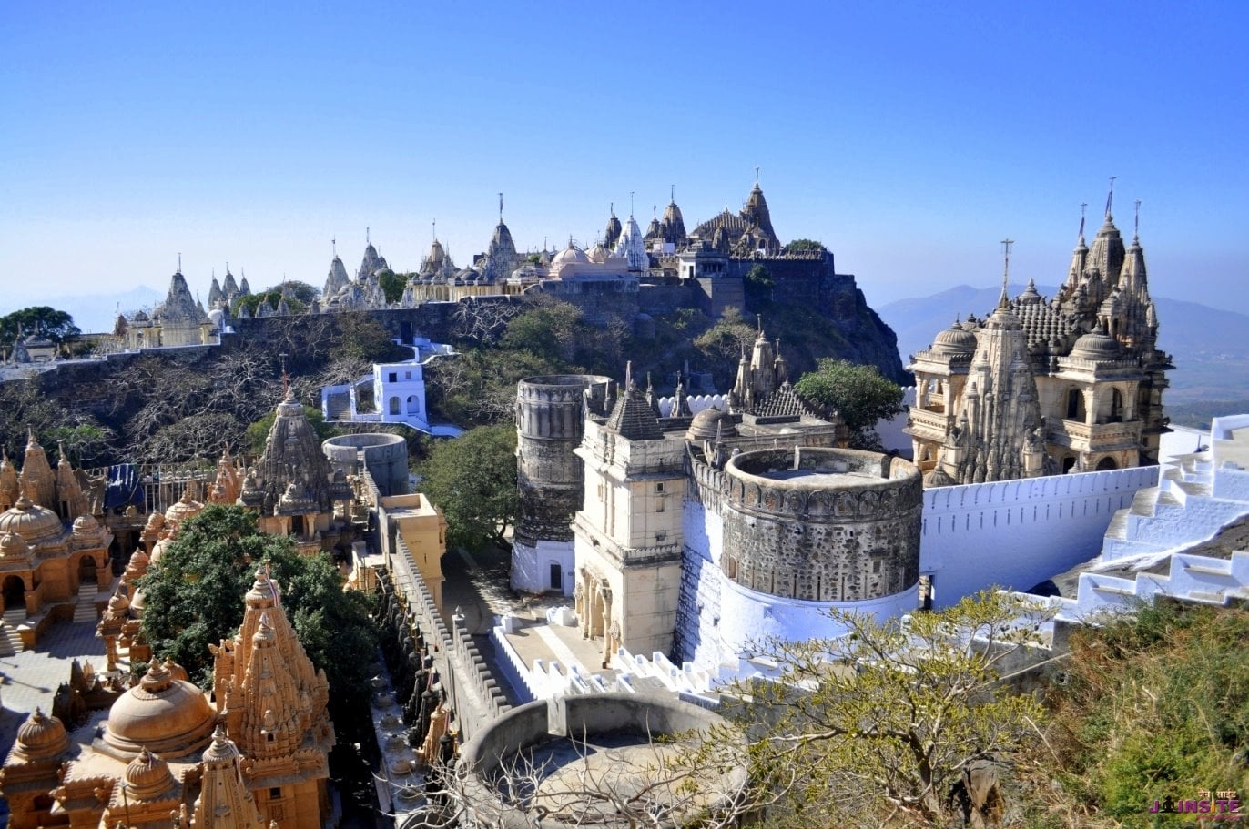 Temple city atop Shatrunjaya hill in Palitana with marble shikhars under a clear blue sky
