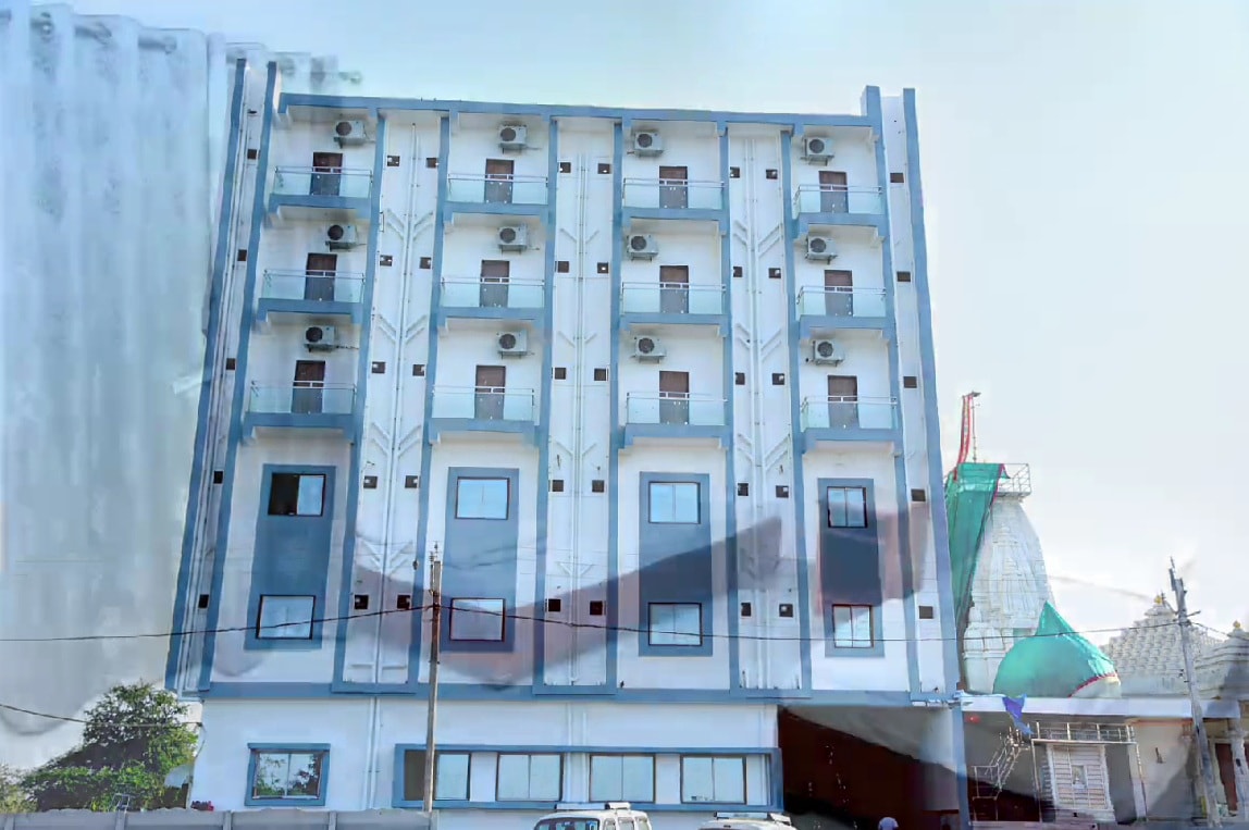 Jainsite Bhavan, a seven-storey white and blue dharamshala with balconies, beside a Jain temple shikhar in Palitana